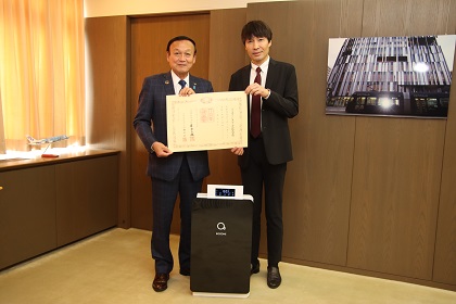 バイオゾーンメディカル株式会社の代表取締役社長と藤井市長。空気清浄機を挟んで記念撮影。